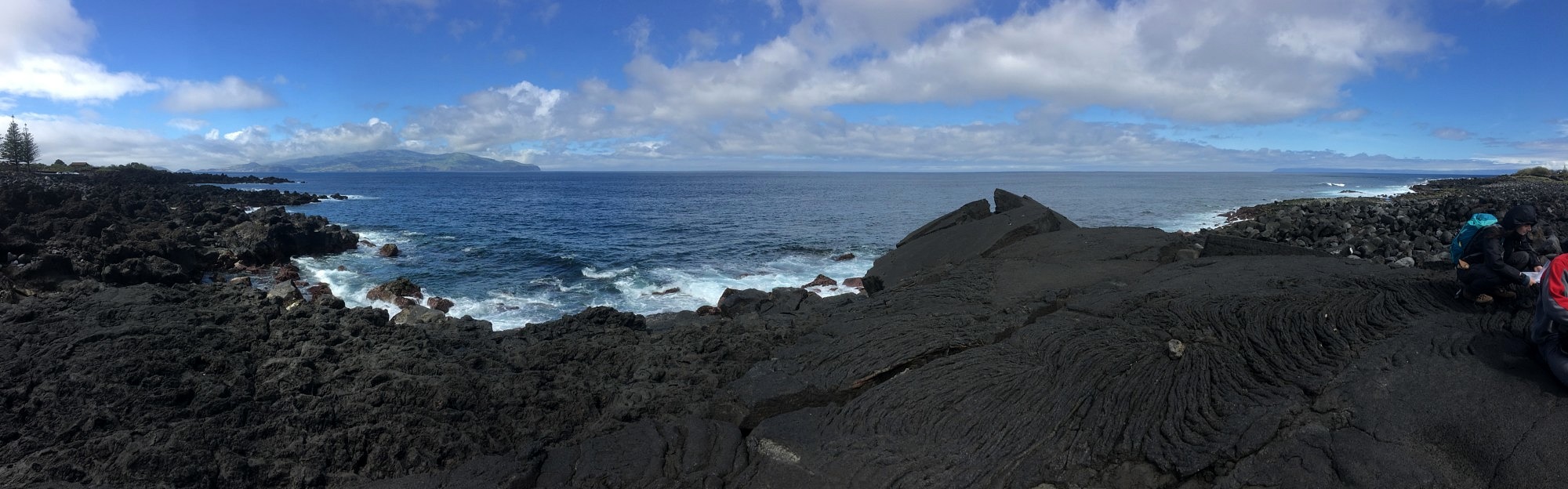 Untersuchung eines jungen Pāhoehoe Lavaflows auf Pico. In der Ferne ist die Insel Faial zu sehen. Im Vordergrund ist deutlich die Stricklava Struktur (ropy structure) zu erkennen.