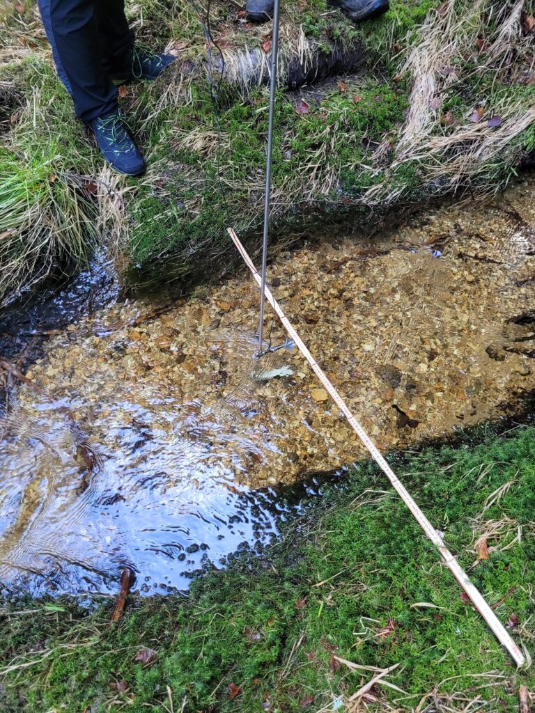 The image shows the Seba M1 mini current meter being used for a discharge measurement in a small stream.